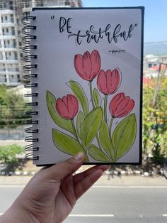 a hand holding up a notebook with flowers drawn on the cover and writing, be beautiful