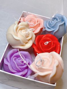 four different colored roses in a box on a white tablecloth with string and ring