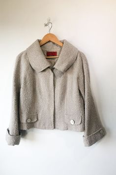 Vintage Carolina Herrera Grey Nubby Wool Jacket. Great condition. Cropped 3/4 sleeve jacket with snap front closure. Has oversized buttons at front faux pockets and cuffs. In allover grey/ivory nubby boucle boiled wool fabric. 54% Acrylic 25% Polyester 19% Wool 2% Nylon. Marked as size 14. Made in Spain. Approx. Measurements: Underarm to Underarm: 20 1/2" Length: 21" Spring Tweed Outerwear With Button Cuffs, Classic Fall Outerwear With 3/4 Sleeve, Tweed Outerwear With Button Cuffs Long Sleeve, Tweed Outerwear With Button Cuffs, Cream Tweed Outerwear With Buttons, Beige 3/4 Sleeve Outerwear For Fall, Boiled Wool Fabric, Boiled Wool, Sleeve Jacket