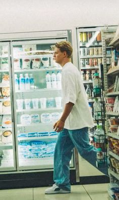 a man walking in front of a refrigerator filled with drinks and water at a grocery store