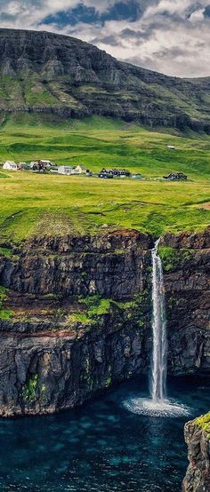 a waterfall in the middle of a large body of water with green grass on both sides