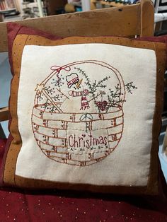 an embroidered pillow with a christmas basket on the front and side, sitting on top of a chair