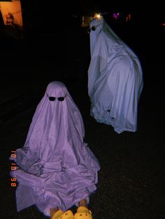 two plastic ghost figures sitting in the middle of a road at night with shoes on them