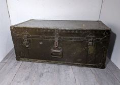 an old trunk is sitting on the floor next to a white wall and wooden floors