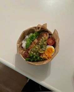 a paper bag filled with food sitting on top of a white table next to a fork