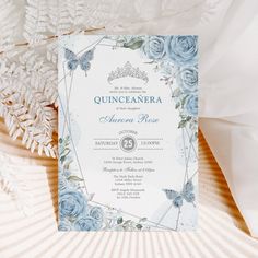 a blue and white wedding card with flowers on it, next to some feathers in the background