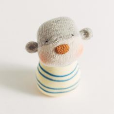 a small stuffed animal with a striped shirt and hat on it's head, sitting in front of a white background