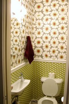 a bathroom with green and white wallpaper, toilet and sink in the doorway way