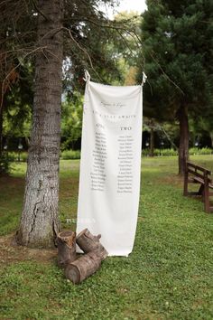 a white banner hanging from the side of a tree in front of a bench and picnic table