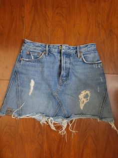 an old jean skirt with torn holes and fraying on the bottom, sitting on a wooden floor