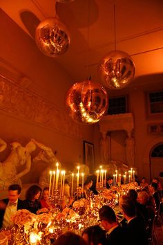 a group of people sitting around a dinner table with candles in front of them and disco balls hanging from the ceiling