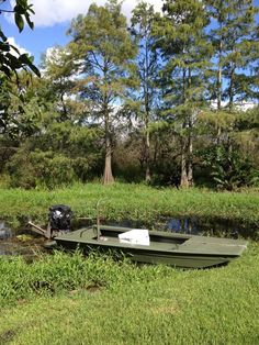 a small green boat sitting on top of a lush green field next to a forest