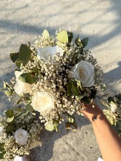 a person holding a bouquet of flowers in their hand on the ground next to sand