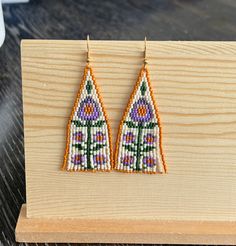 a pair of beaded earrings sitting on top of a wooden board