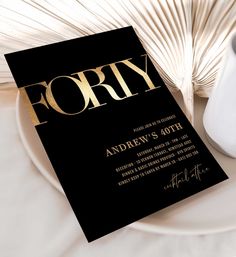 a black and gold party card on a plate next to a white vase with palm fronds