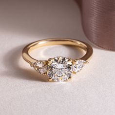 three stone diamond ring on white surface next to pink satine ribbon, closeup