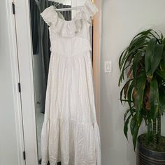 a white dress hanging on a rack next to a potted plant