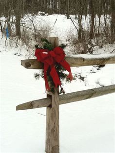 a wooden fence with a red bow on it in the middle of snow covered ground