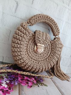 a crocheted handbag sitting on top of a wooden table next to purple flowers