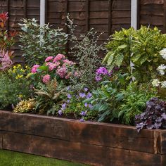 a wooden box filled with lots of different types of flowers and plants next to a fence