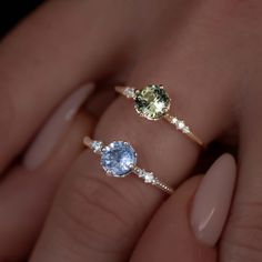 two engagement rings with different colored stones on each one and an oval diamond in the middle