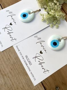 two white and blue eyeball earrings on top of a piece of paper next to a plant