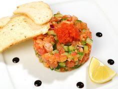 a white plate topped with a salad next to a slice of lemon wedged bread