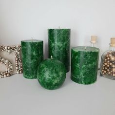 three green candles sitting next to each other on top of a table with ornaments around them