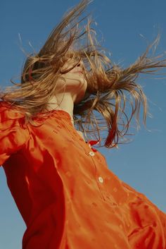 a woman in an orange dress is flying through the air with her hair blowing in the wind