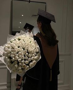 a woman holding a bouquet of white flowers in front of a mirror and wearing a graduation cap