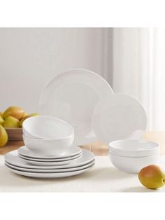 white dishes are stacked on top of each other in front of apples and pears