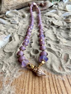 "Add a touch of grace to your ensemble with this Shell Charm Stretched Necklace! Crafted with utmost care, this necklace showcases a beautiful combination of lavender and iridescent purple glass beads, elegantly strung together to create a captivating design. The addition of gold bead caps, spacers, and a shell charm lends a whimsical touch, making it a must-have statement piece for any jewelry lover. Whether you're dressing up for a special event or simply want to elevate your everyday style, this necklace is the perfect accessory to complete your look.  Beads may vary in texture and size.  Includes a clean cloth and a small freebie gift. Full Length is 20\" Charm Dangle Length is \". Charm can be made to be removable and lobster clasp can be added upon request(please put it in the person Adjustable 8mm Bead Necklaces For Beach, Faceted Crystal Necklaces With Round Beads For Beach, Spiritual 8mm Beads Jewelry For Beach, Spiritual Beach Necklace With Colorful Beads, Hand-strung Purple Jewelry For Beach, Colorful Glass Bead Jewelry For Beach, Beaded Czech Glass Jewelry For Beach, Czech Glass Necklaces With Round Beads For Beach, Hand-strung Purple Beach Jewelry