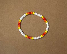 a beaded bracelet with white, yellow and red beads sits on a brown surface