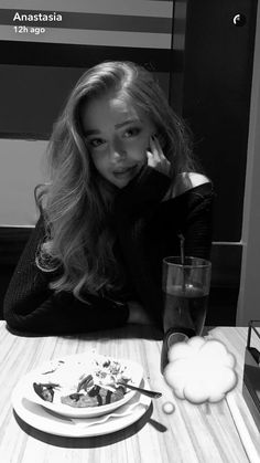 a woman sitting at a table in front of a plate of food and a drink