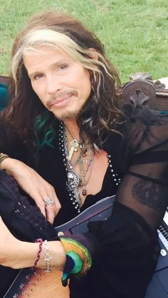 a man with long hair sitting in a chair next to a green grass covered field