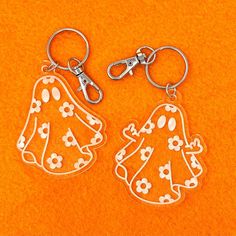 two plastic keychains with white designs on them sitting on an orange surface next to each other