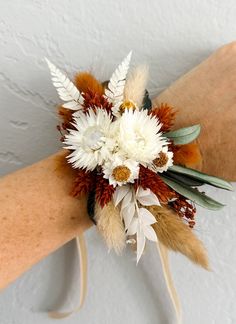 a woman's arm holding a bouquet with flowers and feathers on it in front of a white wall