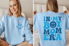 a woman wearing a blue sweatshirt with the words in my box mom era printed on it