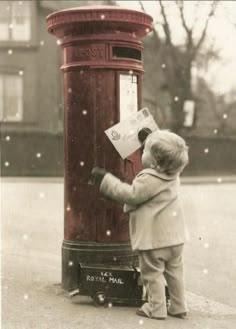 a little boy standing in front of a red post box holding a piece of paper