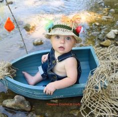 a baby sitting in a small blue boat on the water with a fishing pole sticking out of it's mouth