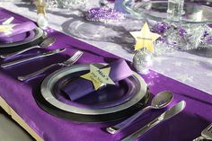 a purple table setting with silverware and star place settings on the napkins,