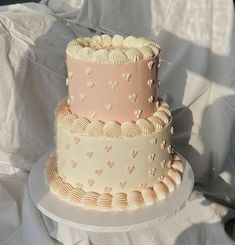 two tiered cake with hearts on it sitting on a plate next to a white sheet