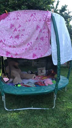 a teddy bear sitting on top of a green trampoline covered in pink and white fabric