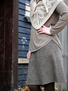 a woman standing in front of a blue building wearing a sweater and skirt with a scarf around her neck