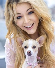 a woman holding a small white dog in her arms and smiling at the camera with long blonde hair