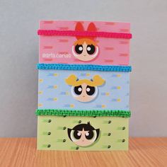 three little boxes with cartoon characters on them sitting on top of a wooden table in front of a gray wall