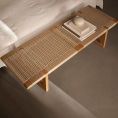 a wooden table with a bowl on top of it next to a white bed and pillows