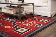 a cat sitting on top of a red rug next to a white couch and coffee table