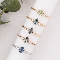 five rings with different colored stones on them sitting on a white napkin next to a plant