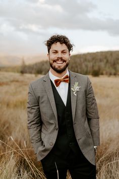 a man wearing a suit and bow tie standing in tall grass with his hands in his pockets